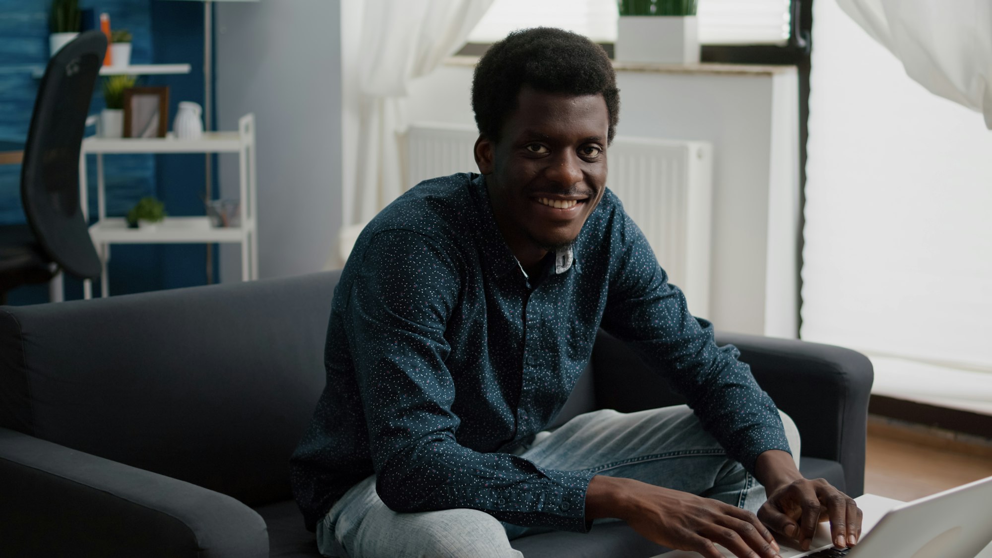 Portrait of black man in living room typing on laptop